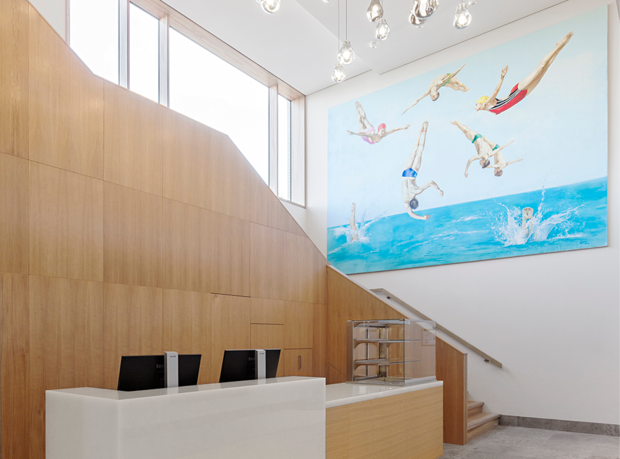 Eingangsbereich mit großem Holztreppengeländer bzw. Verkleidung. Außerdem sieht man eine Rezeption aus Holz.