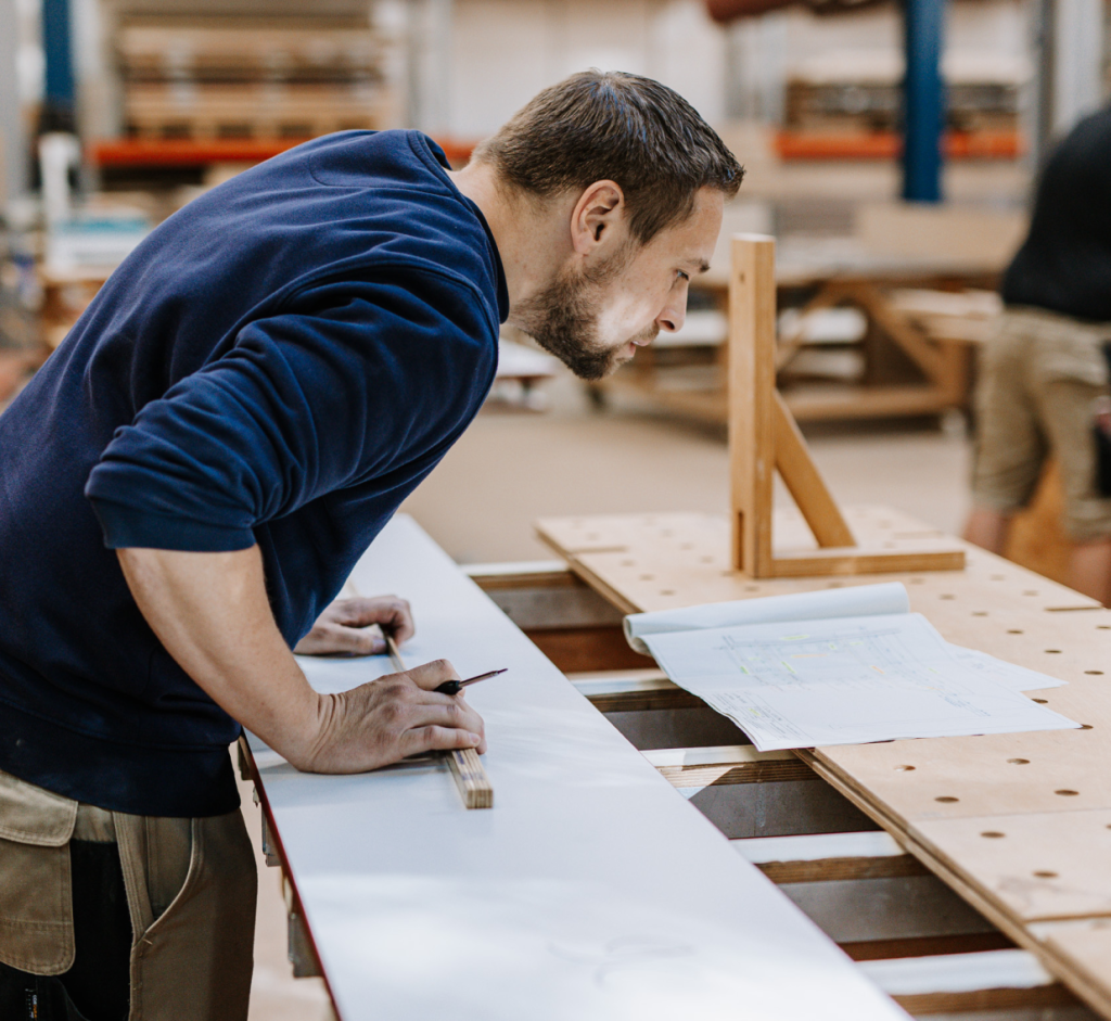 Mitarbeiter misst etwas aus und schaut dabei auf seine Pläne.