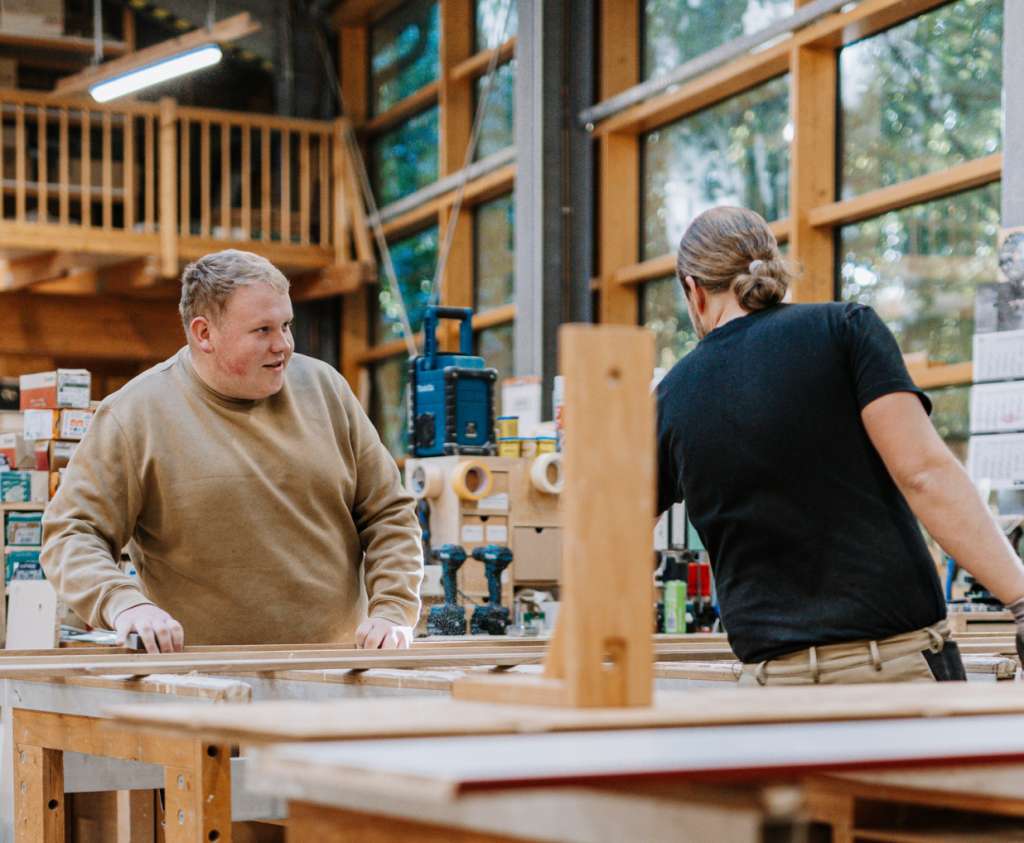 Zwei Mitarbeiter stehen in der Tischlerei vor einem Projekt und tauschen sich darüber aus.